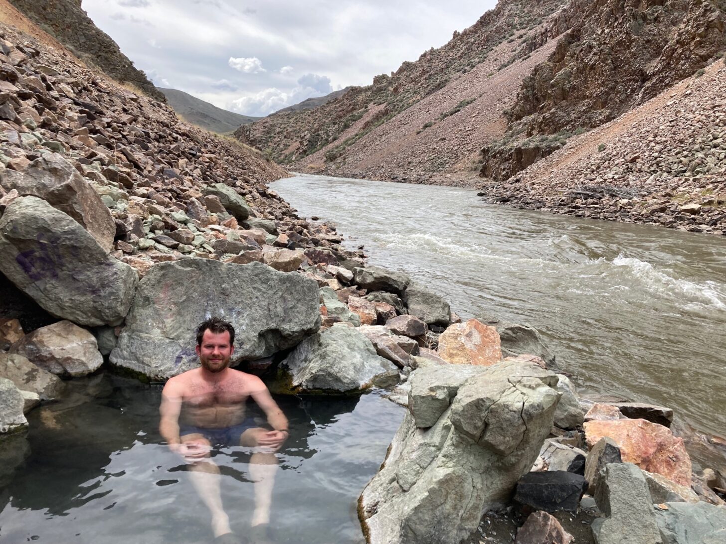 A man sits in a hot spring next to a river.