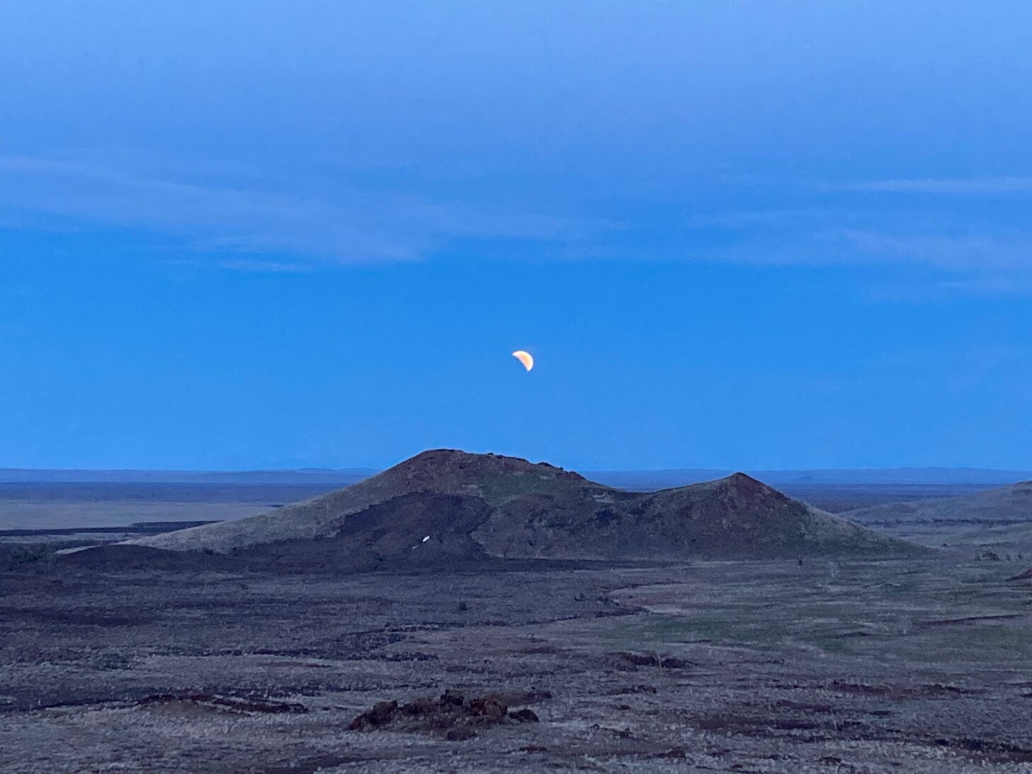 A moon in the early phases of a lunar eclipse is shown above a stark landscape.