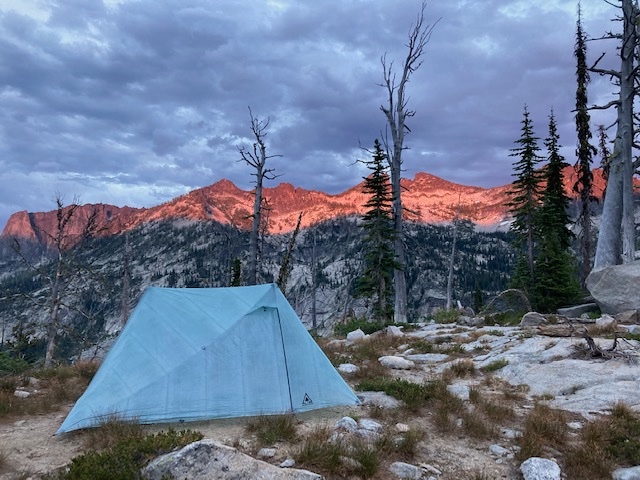 tent pitched at a rocky campsite near the treeline, sunset alpenglow over the mountains in the background