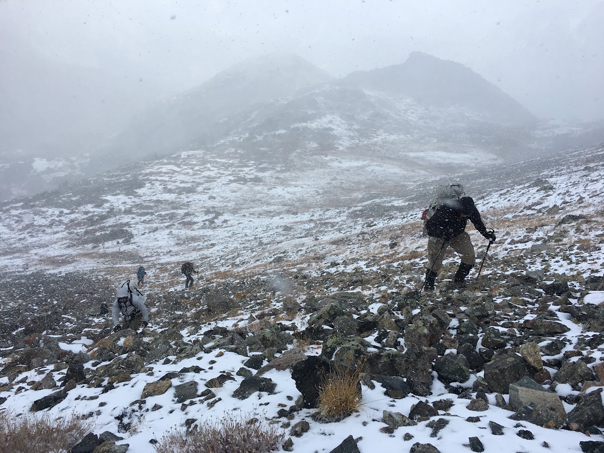 four people climb up a steep slope in the middle of a snowstorm.