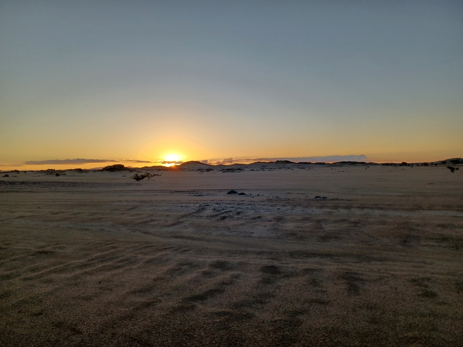 the sun is setting over a sandy beach