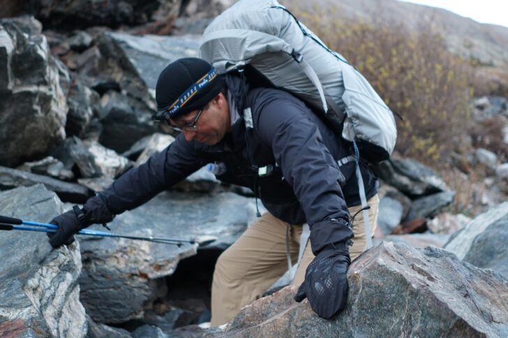 A man scrambles up a field of talus while wearing a backpack
