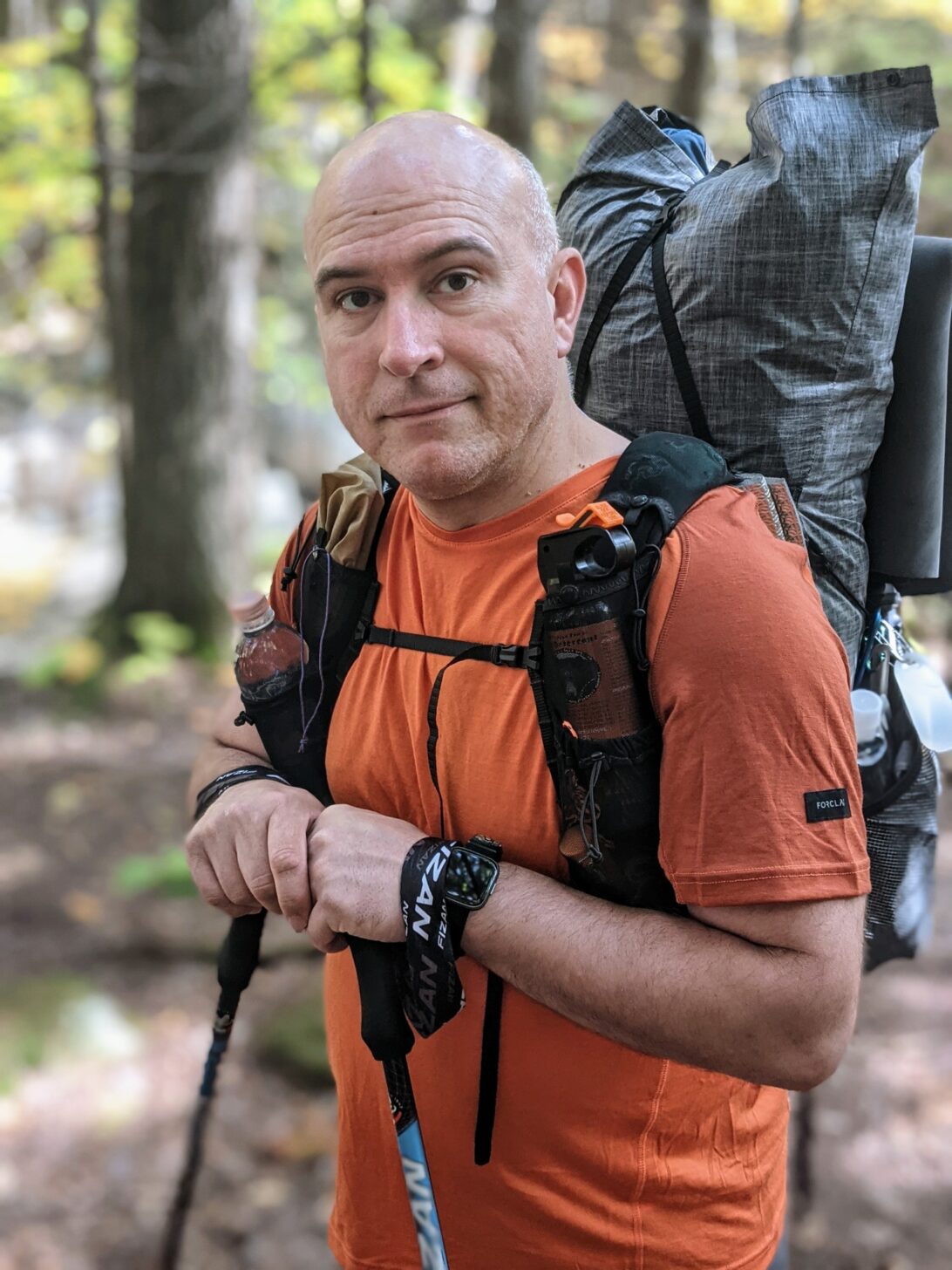 a medium shot of a man wearing a backpack with shoulder strap pockets. The shoulder strap pockets contain gear and a water bottle.