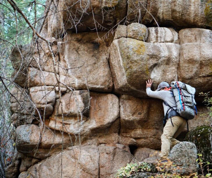 a man scrambles along a rock face wearing a backpack