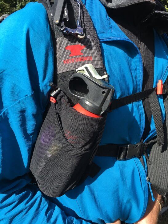 a close-up of a backpack with shoulder-strap pockets. In one of the pockets is a container of bear spray.