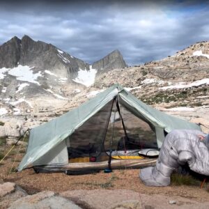 man drinking coffee by a tent in the mountains