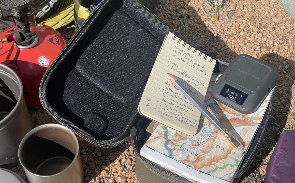 satellite messenger with notebook, pencil, coffee, map, and stove