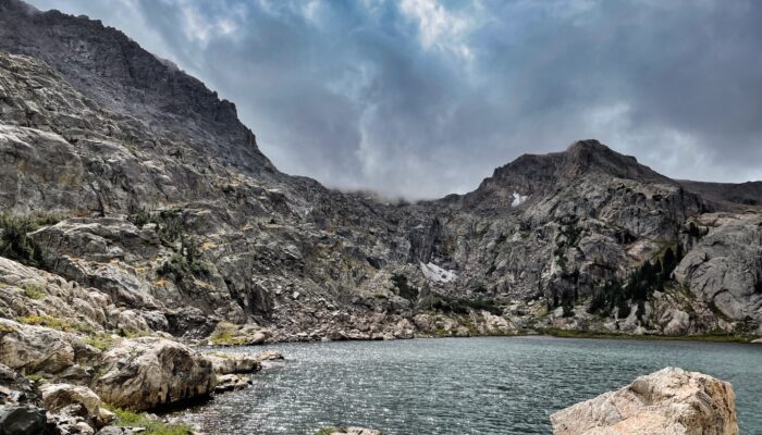 a lake surrounded by mountains under a cloudy sky