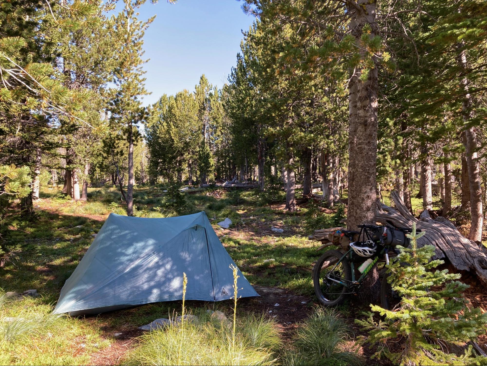 a tent pitched up in the woods next to a motorcycle