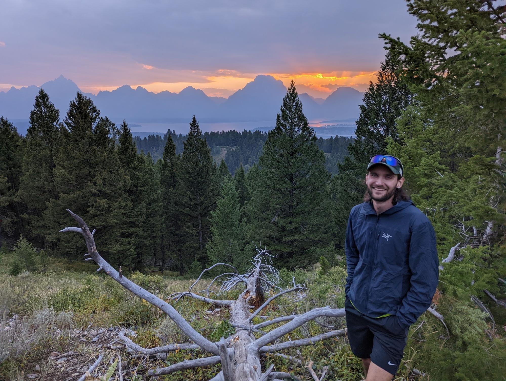 a man standing next to a fallen tree in a forest