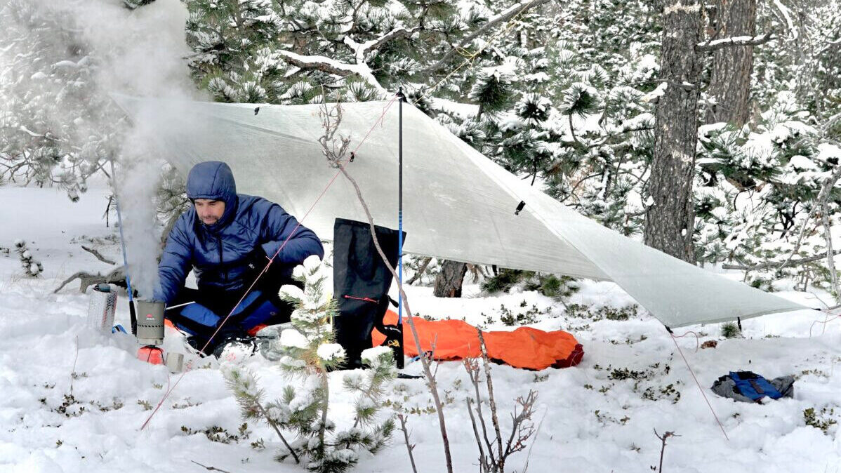 hiker cooking under tarp in snow