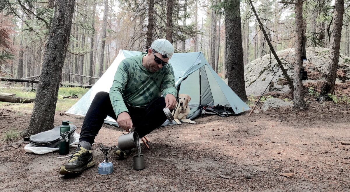 man sitting by a tent brewing coffee