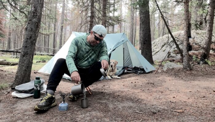 man sitting by a tent brewing coffee