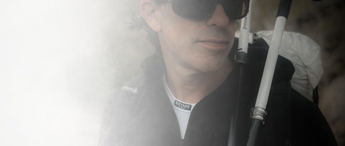 hiker wearing a fishnet base layer under another layer, carrying a pack and trekking poles