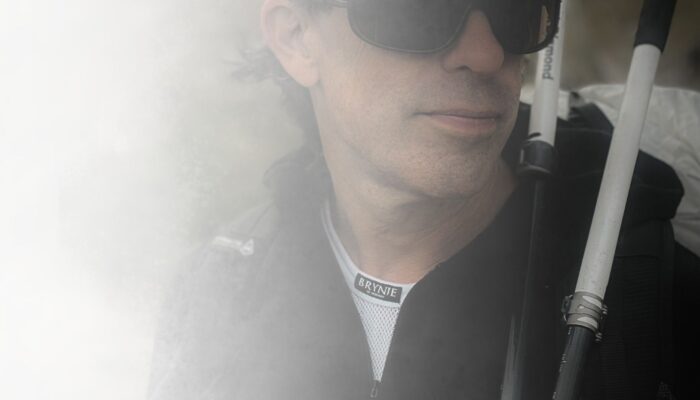 hiker wearing a fishnet base layer under another layer, carrying a pack and trekking poles