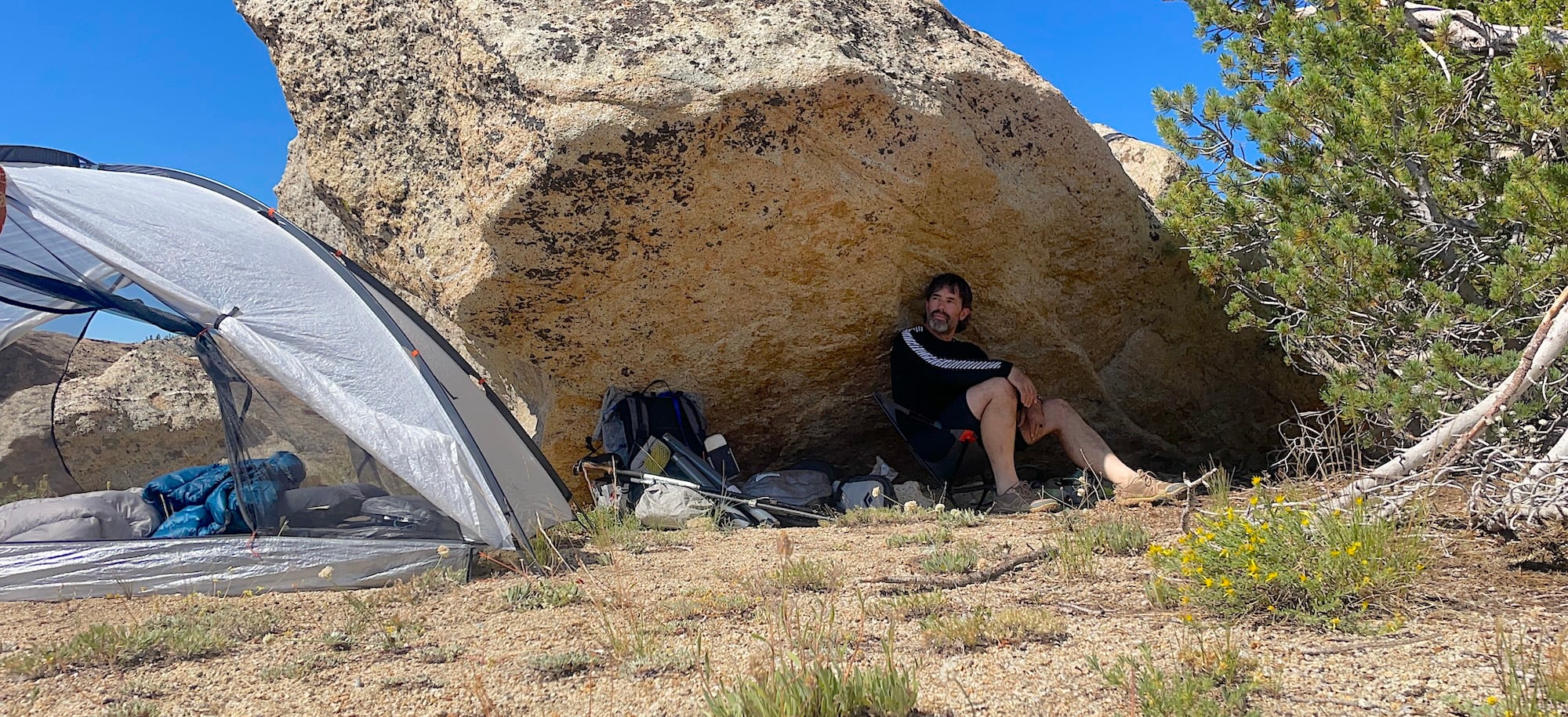 hiker seeking shade under a rock at a campsite