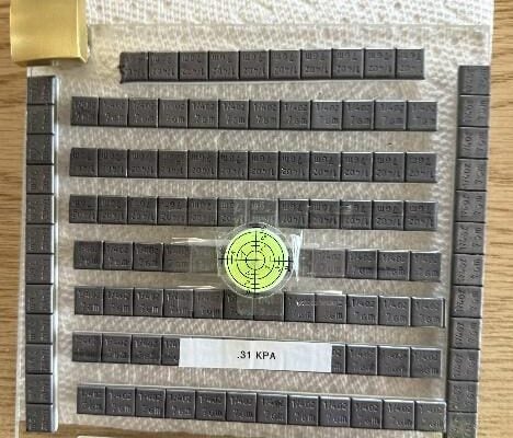 A grid of stacked metal plates, each labeled with measurements and codes, arranged on a wooden surface.AI-generated content may be incorrect.