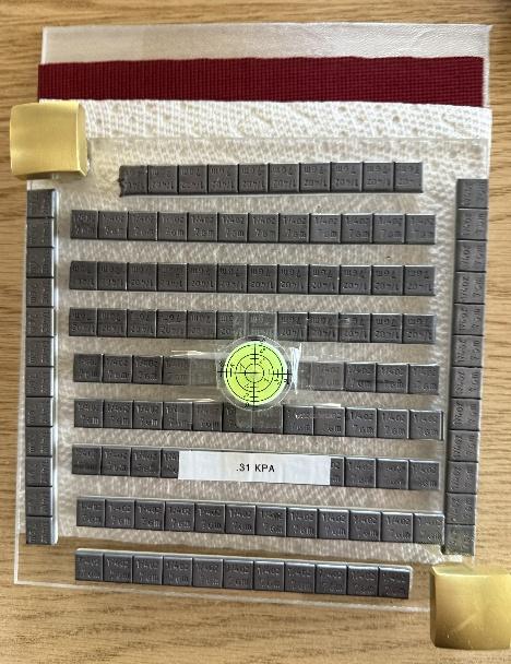 A grid of stacked metal plates, each labeled with measurements and codes, arranged on a wooden surface.AI-generated content may be incorrect.
