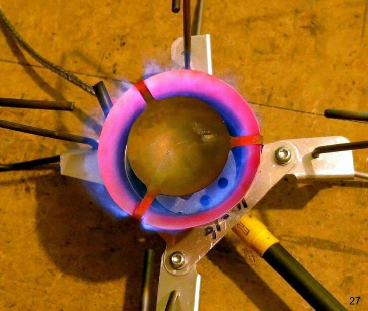 Top view of a prototype stove with glowing burner ring and blue flame.